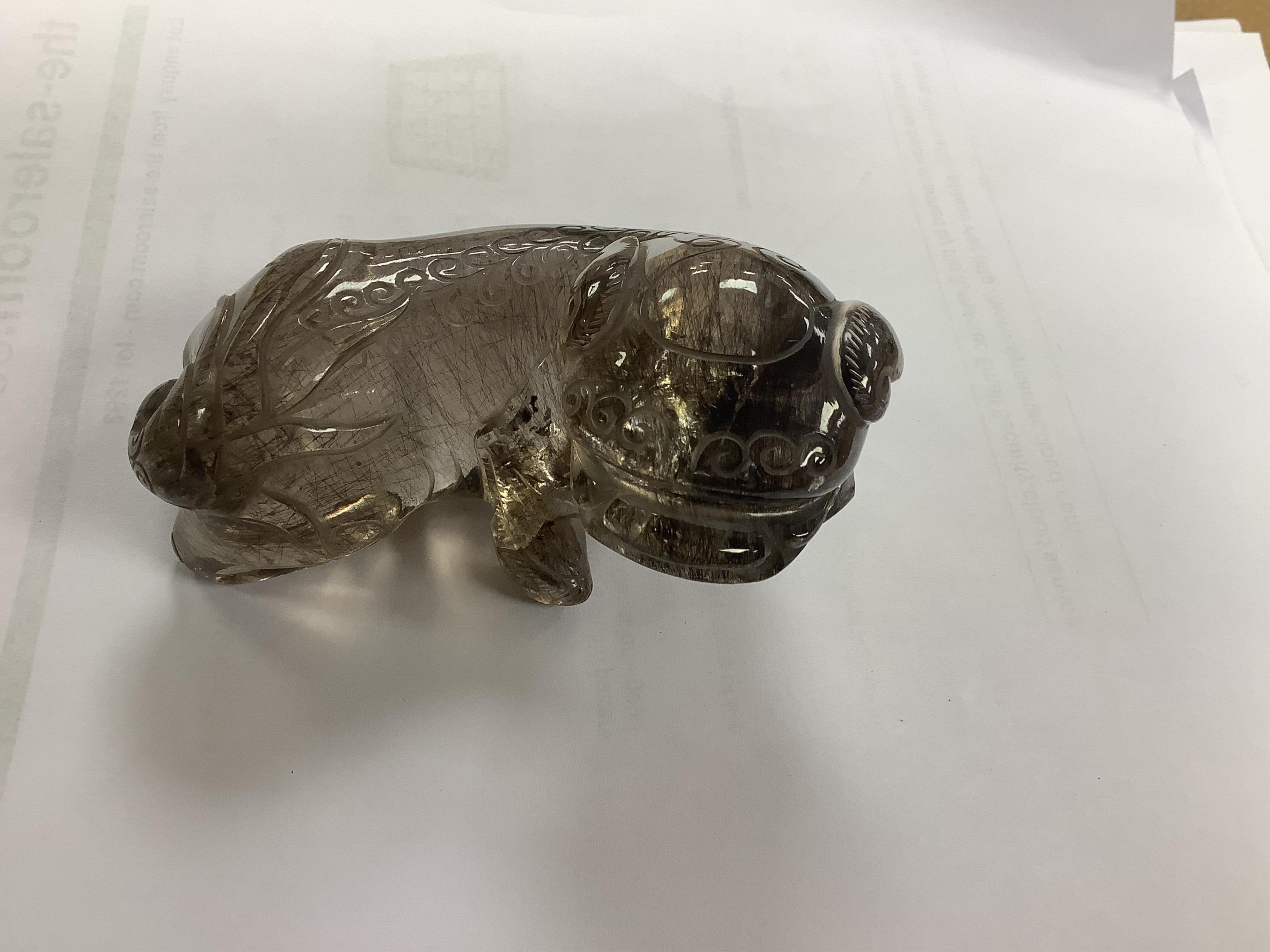 A Chinese carved smoky quartz lion dog on hardwood stand, 9.5cm wide. Condition - fair, impact damage to tail